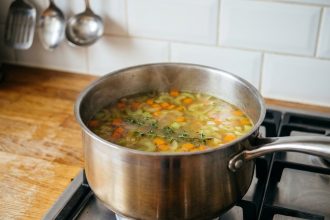 Casserole en inox sur feu de gaz avec un bouillon maison doré aux légumes frais et thym